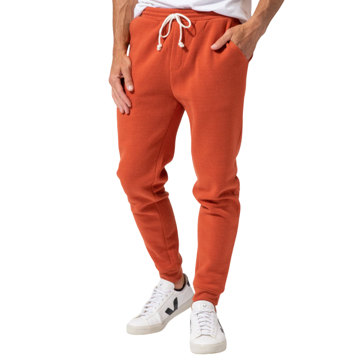A person is wearing orange jogger pants with a drawstring waist, paired with white sneakers featuring a black logo.