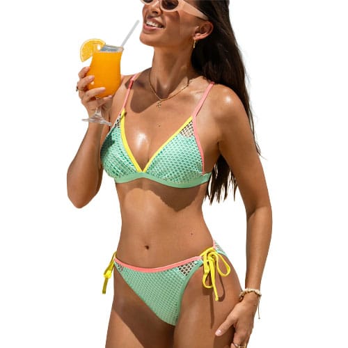 A woman wearing a colorful mesh bikini, holding a glass of orange juice with a straw. The bikini features light blue and yellow with pink trim, and the top and bottoms have a tied design.
