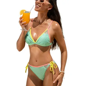 A woman wearing a colorful mesh bikini, holding a glass of orange juice with a straw. The bikini features light blue and yellow with pink trim, and the top and bottoms have a tied design.