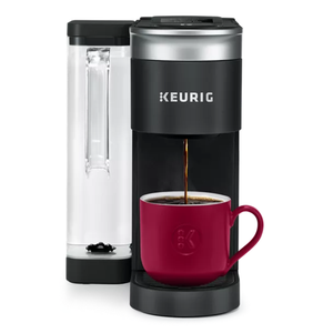 A Keurig K-Supreme coffee maker with a water reservoir is brewing coffee into a red mug. The machine is black with a silver top and has the Keurig logo.
