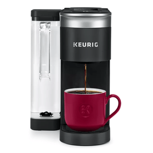 A Keurig K-Supreme coffee maker with a water reservoir is brewing coffee into a red mug. The machine is black with a silver top and has the Keurig logo.
