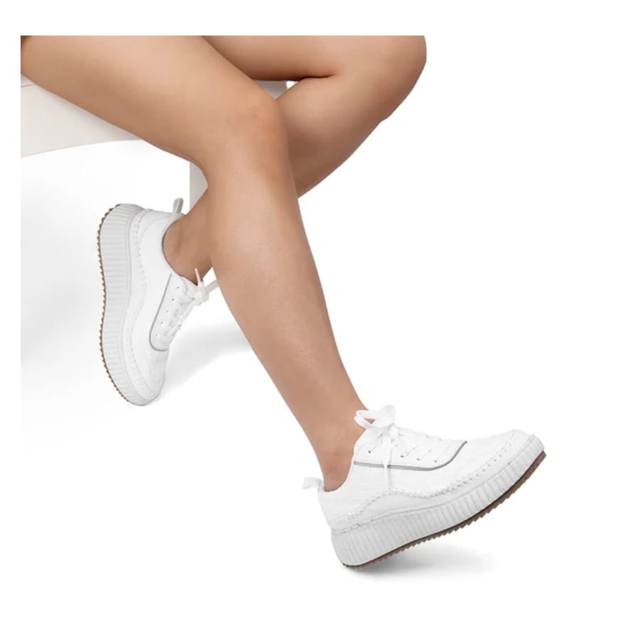 A pair of white platform sneakers worn by a person seated with legs crossed.