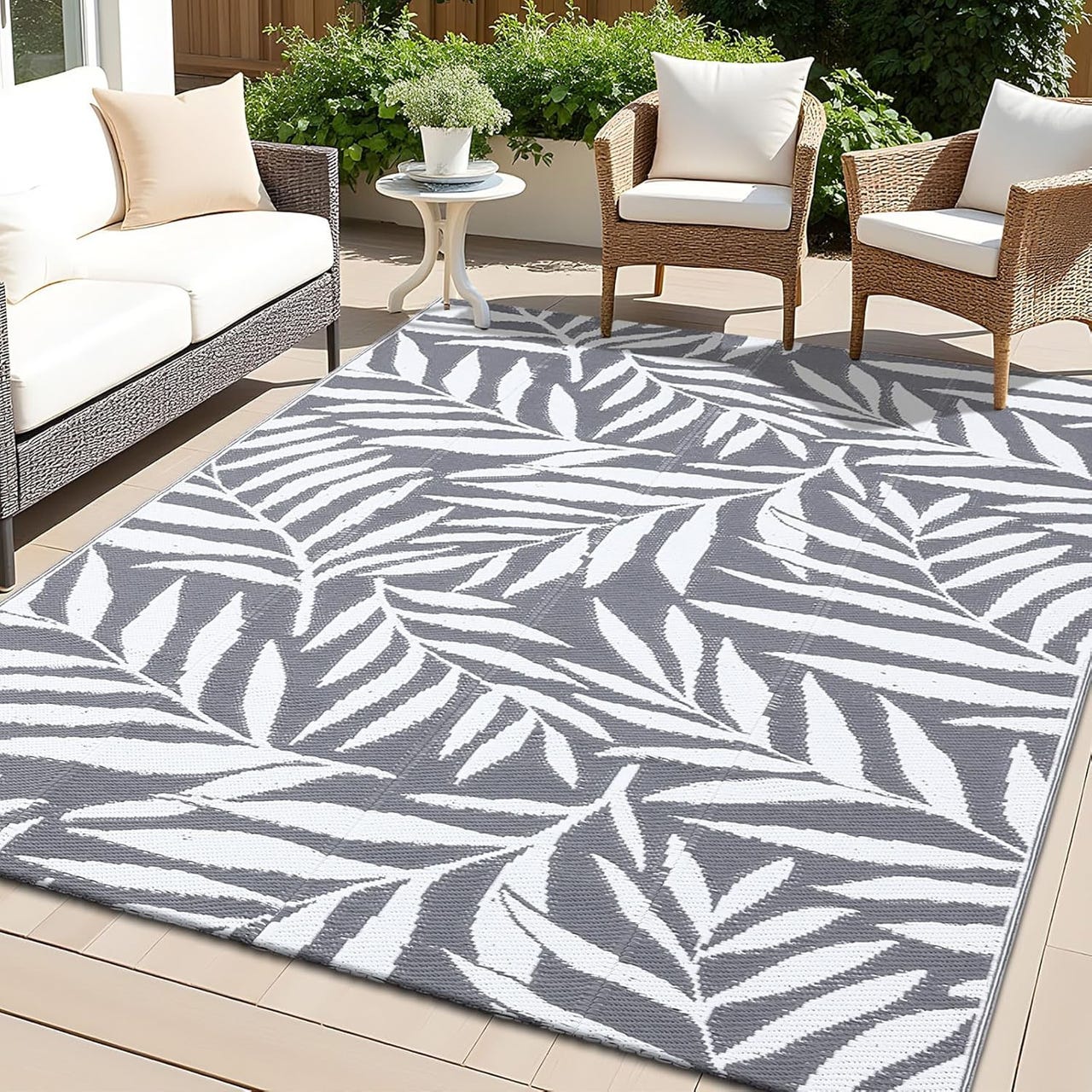 A 5' x 8' outdoor rug featuring a white leaf print on a gray background, placed on a patio with wicker furniture.
