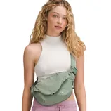A woman models a white sleeveless halter top and pink drawstring pants, wearing a light green crossbody bag.