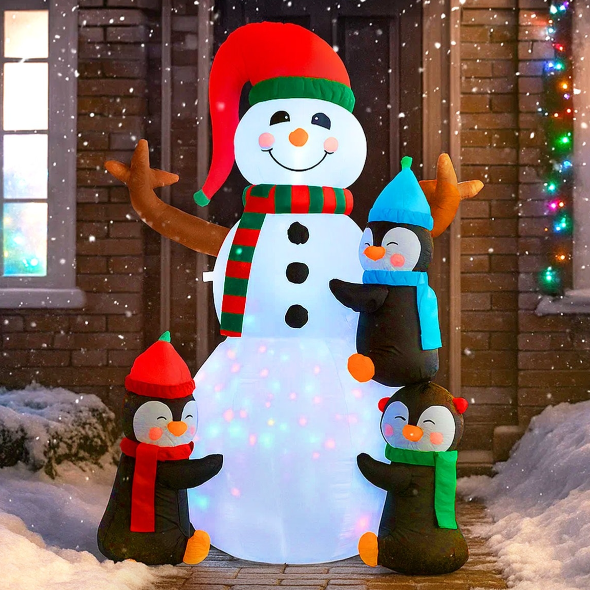 Inflatable snowman with penguins, featuring a large snowman with a red hat and scarf, accompanied by three penguins wearing colorful accessories, set against a snowy backdrop with holiday lights.