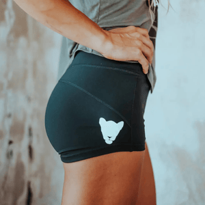 Black athletic shorts with a white minimalist animal face logo on the side, worn by a person with a hand on their hip.