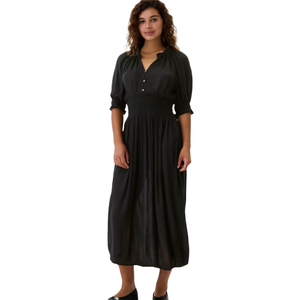 A woman wears a long, black button-up dress with a cinched waist and three-quarter sleeves, paired with matching black shoes.