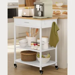 A white kitchen cart with a wooden top holds a coffee machine, a drawer, and two shelves featuring utensils, jars, a woven basket, and a bowl of bananas, with a green towel hanging on the side. The cart is on wheels for mobility.