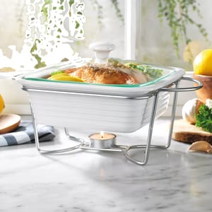 White ceramic chafing dish with a lid placed on a metal stand, kept warm by a tealight candle underneath.