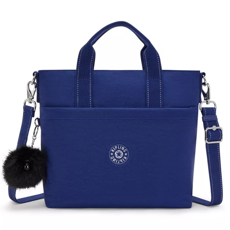 Blue tote bag with dual handles, detachable crossbody strap, front pocket, and a fluffy black charm. Features a circular logo design.