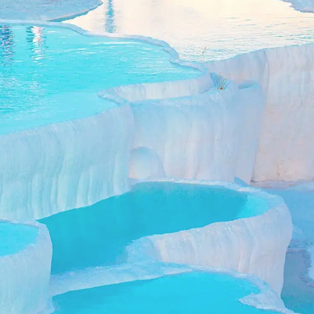 Natural thermal pools with clear turquoise water forming terraces on a white mineral-rich surface.