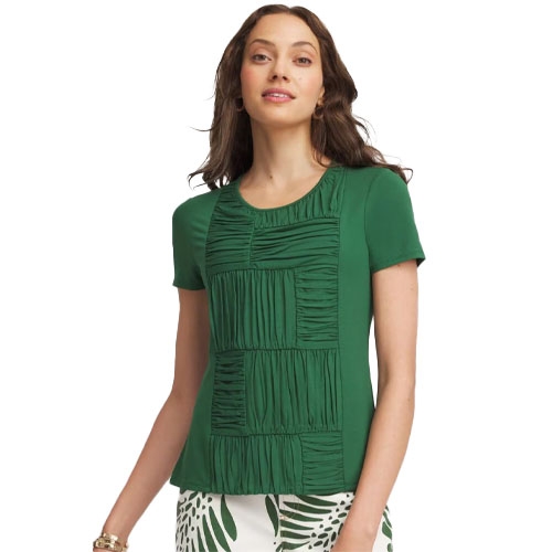 Woman wearing a green short-sleeve top with textured square patterns on the front, paired with white pants featuring green leaf prints.