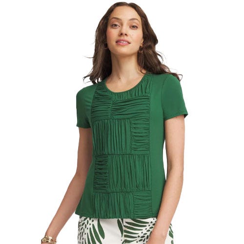 Woman wearing a green short-sleeve top with textured square patterns on the front, paired with white pants featuring green leaf prints.