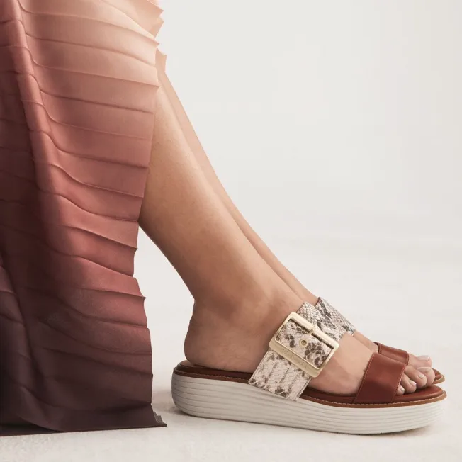 A person's foot wearing a wide-strapped platform sandal with snake-skin texture and a metallic buckle.