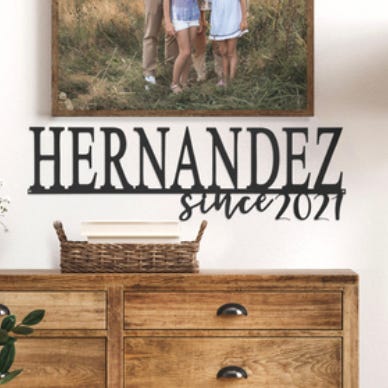 Wall decor sign with \“HERNANDEZ since 2021\“ text displayed above a wooden dresser with a photo of a family on the wall.