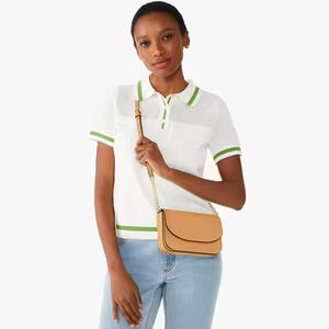 A woman wearing a white polo shirt with mesh details, light blue jeans, and a small tan crossbody bag with a chain strap.