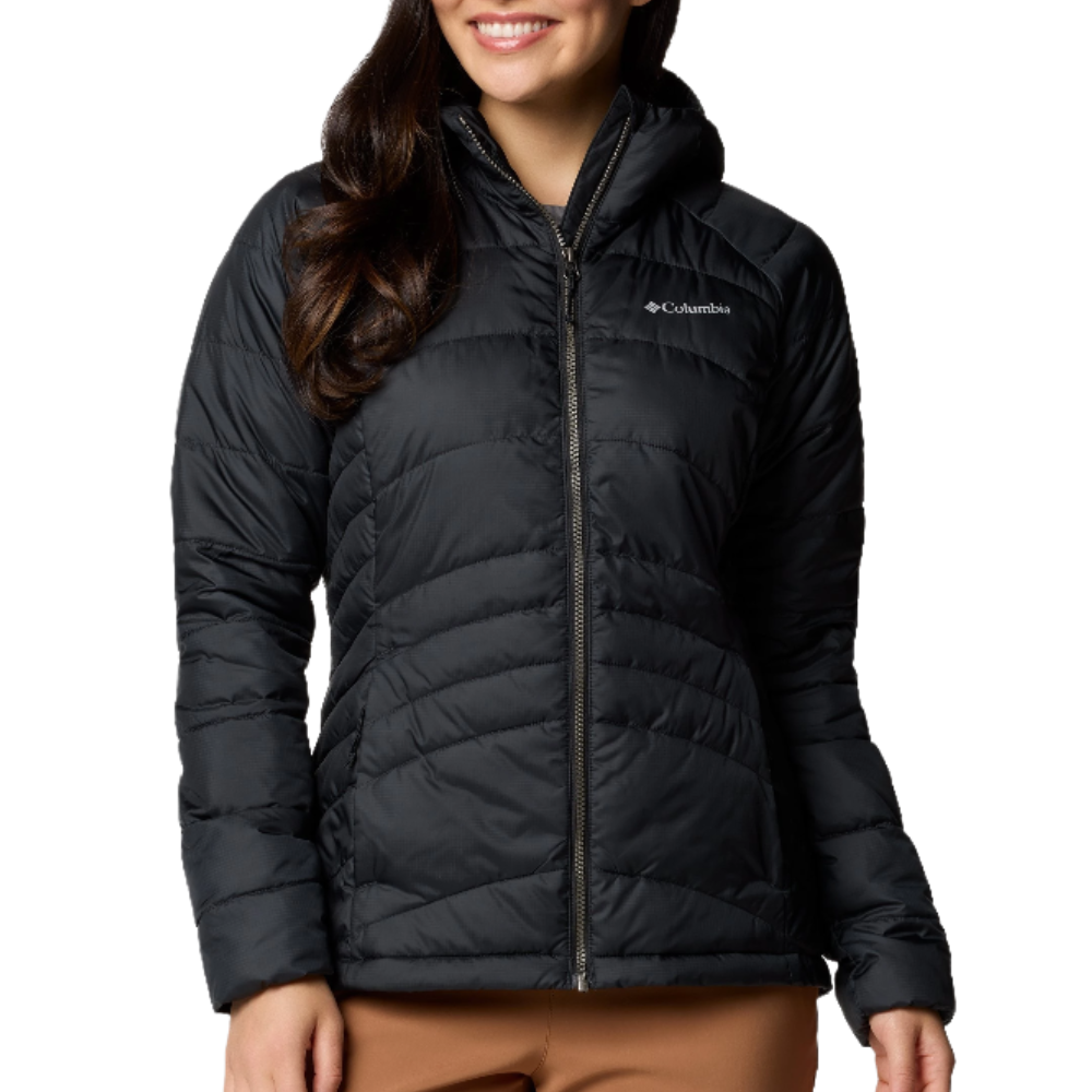A woman is wearing a black Columbia puffer jacket with a front zipper and hood, paired with brown pants.