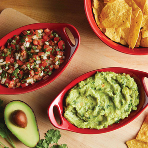 Red serving dishes contain pico de gallo, guacamole, and tortilla chips, with half an avocado and cilantro on the side.