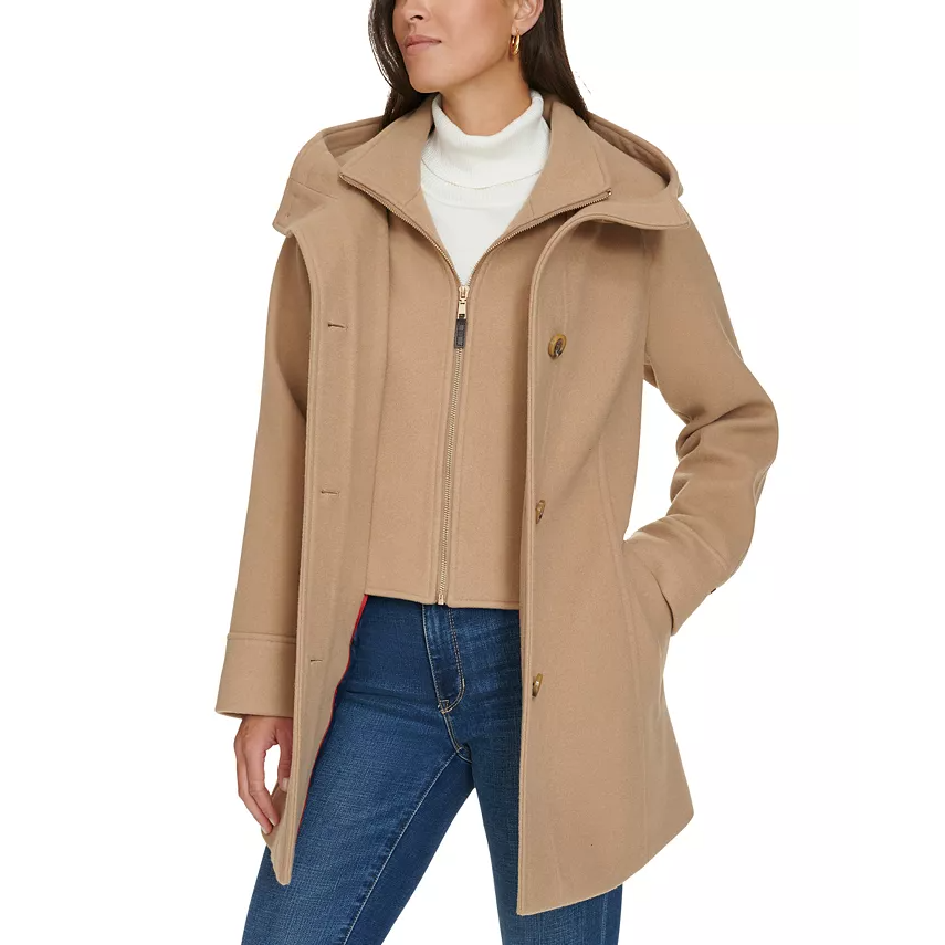 A beige Tommy Hilfiger lined hooded coat features a front zip closure, button detailing, and a relaxed fit. Paired with a white turtleneck sweater and jeans, it offers a stylish and practical design for cooler weather.