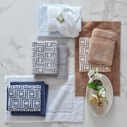 Assorted bath towels in different colors and patterns are neatly arranged on a marble surface, accompanied by a small dish with soap and decorative flowers.