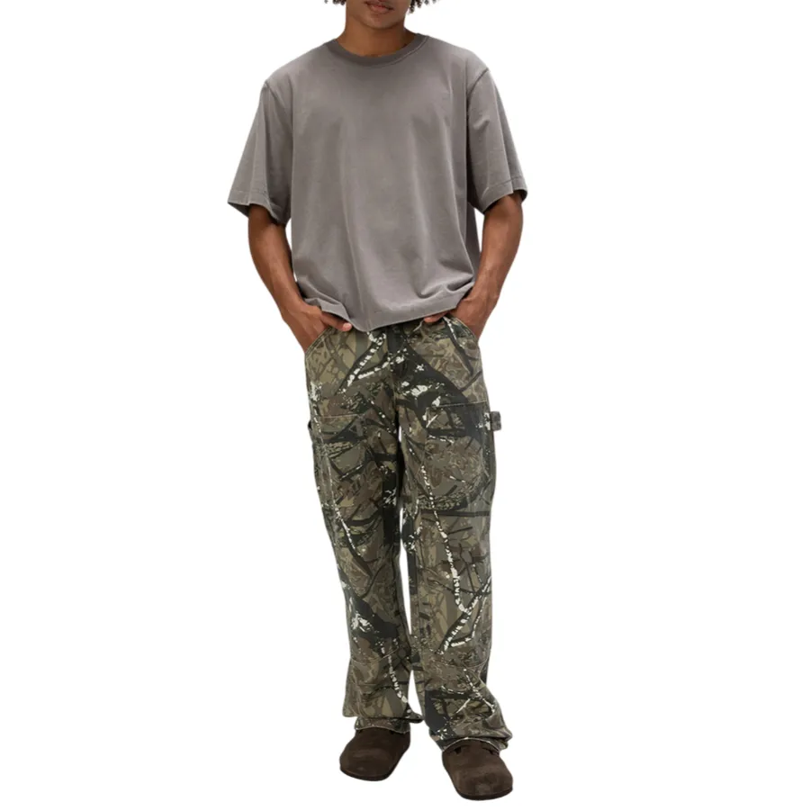 A person is wearing a loose gray T-shirt paired with camouflage cargo pants and dark brown slip-on shoes, standing against a plain background.