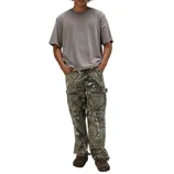 A person is wearing a loose gray T-shirt paired with camouflage cargo pants and dark brown slip-on shoes, standing against a plain background.