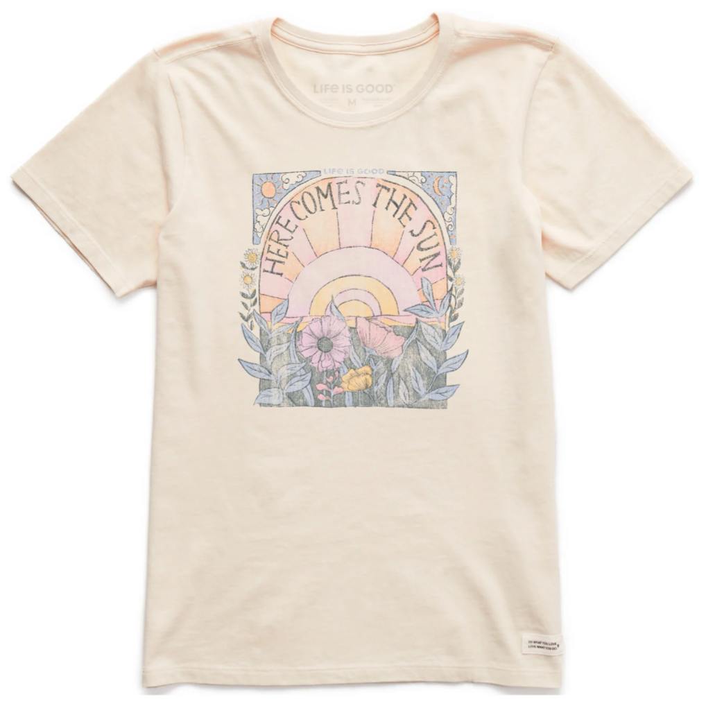 Cream-colored T-shirt featuring a \“Here Comes the Sun\“ graphic with a sunburst, flowers, and foliage design.