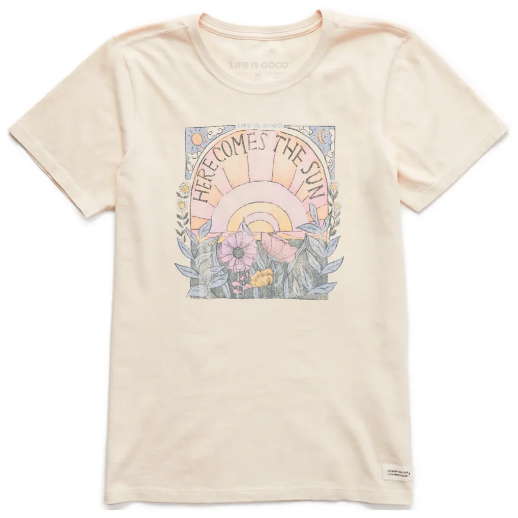 Cream-colored T-shirt featuring a \“Here Comes the Sun\“ graphic with a sunburst, flowers, and foliage design.