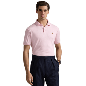 A man wearing a light pink polo shirt with a small embroidered logo on the chest pairs it with dark, pinstriped trousers.
