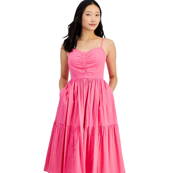 A woman is wearing a pink sleeveless sundress with spaghetti straps and a ruched bodice. The dress features a tiered skirt and is knee-length, showcasing a casual and feminine style.