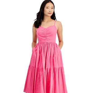 A woman is wearing a pink sleeveless sundress with spaghetti straps and a ruched bodice. The dress features a tiered skirt and is knee-length, showcasing a casual and feminine style.