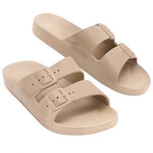 Beige slip-on sandals with two adjustable buckle straps and a textured footbed.