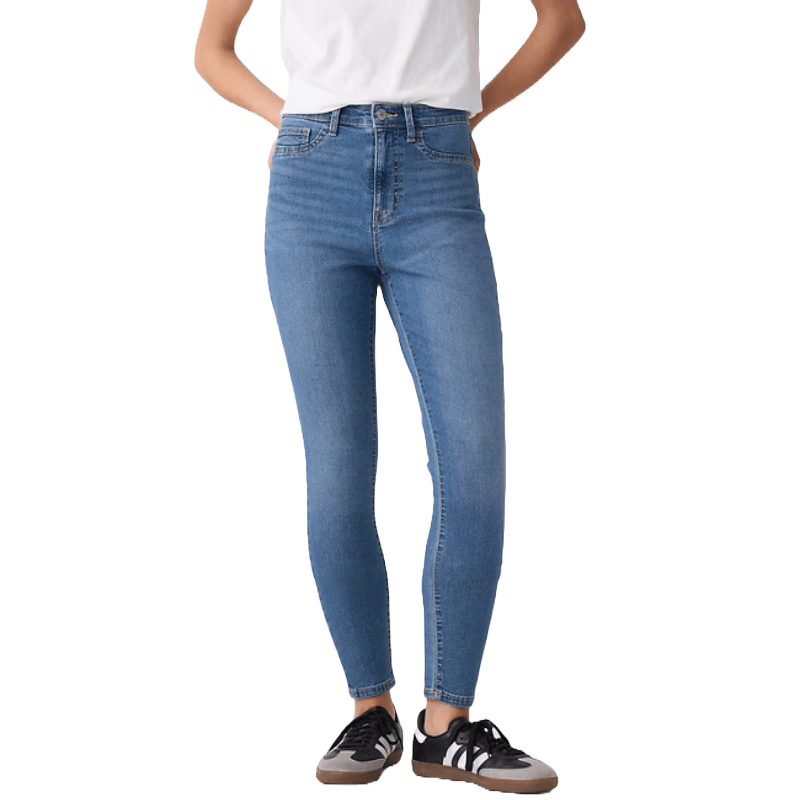 High-rise, medium blue jeggings with a stretchy fit, featuring a button and zip closure. Worn with a white top and black sneakers with white stripes.