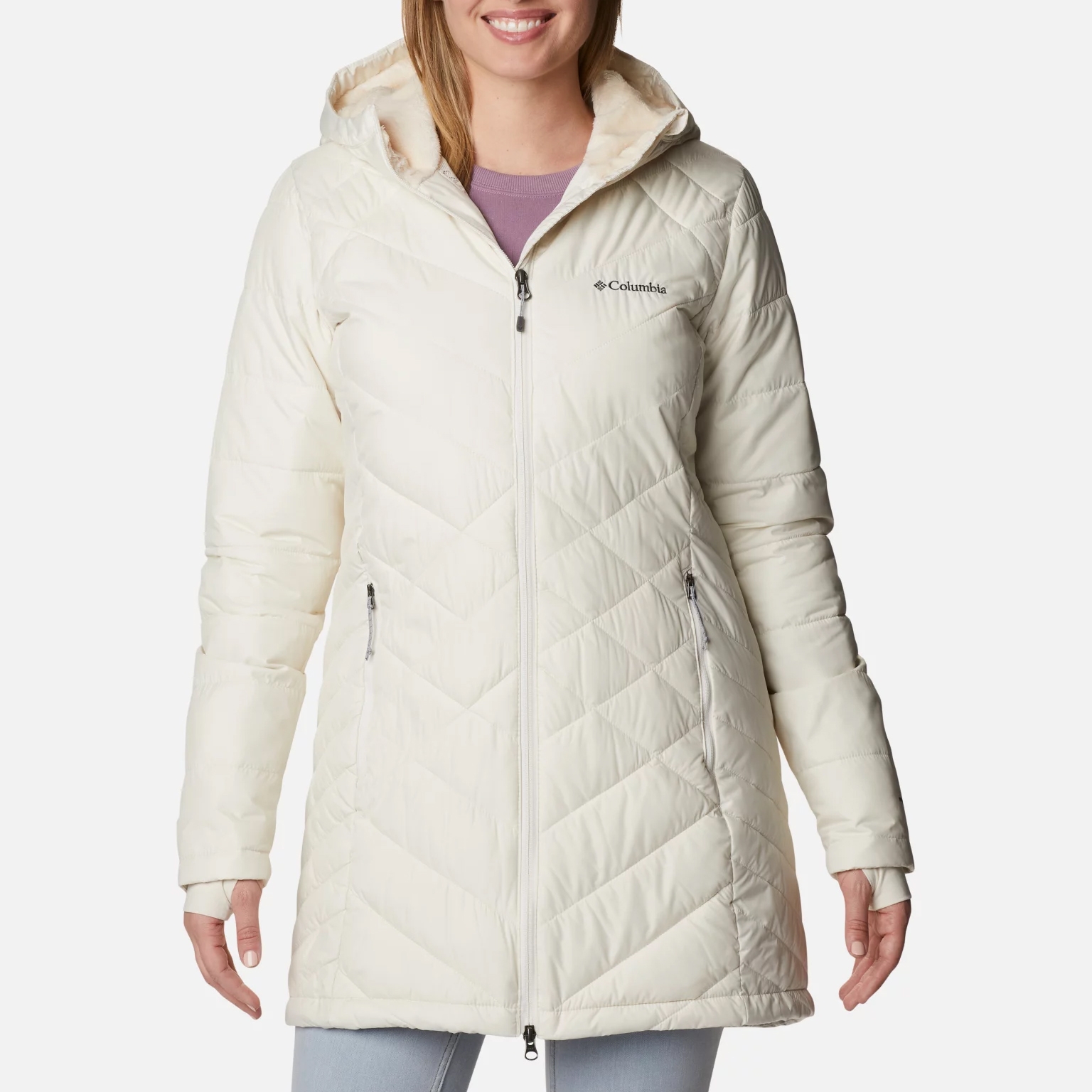 A woman is wearing a light-colored quilted Columbia jacket with a hood and zippered pockets.