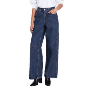 A person is wearing dark blue, wide-leg jeans paired with a white shirt and black boots.