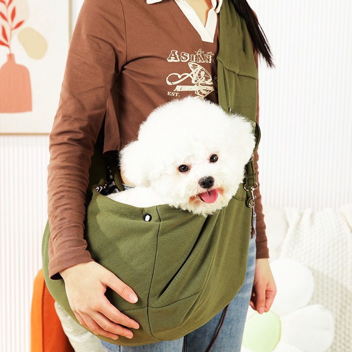 A person carries a fluffy white dog in a green pet sling bag. The bag is worn crossbody, allowing the dog to comfortably sit and peek out.
