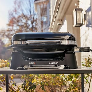 The Weber Lumin Electric Outdoor Grill features a sleek black design with a compact build, ideal for grilling on smaller patios or balconies. It has a stainless steel handle and side control knob for easy temperature adjustments.