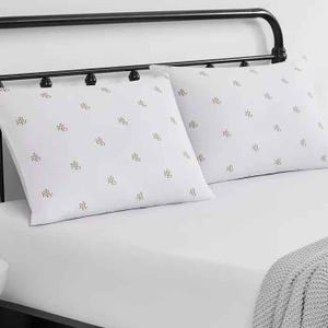 Two white pillows with \“RL\“ initials are set on a bed with a black metal headboard. A gray knitted blanket is draped at the foot of the bed.