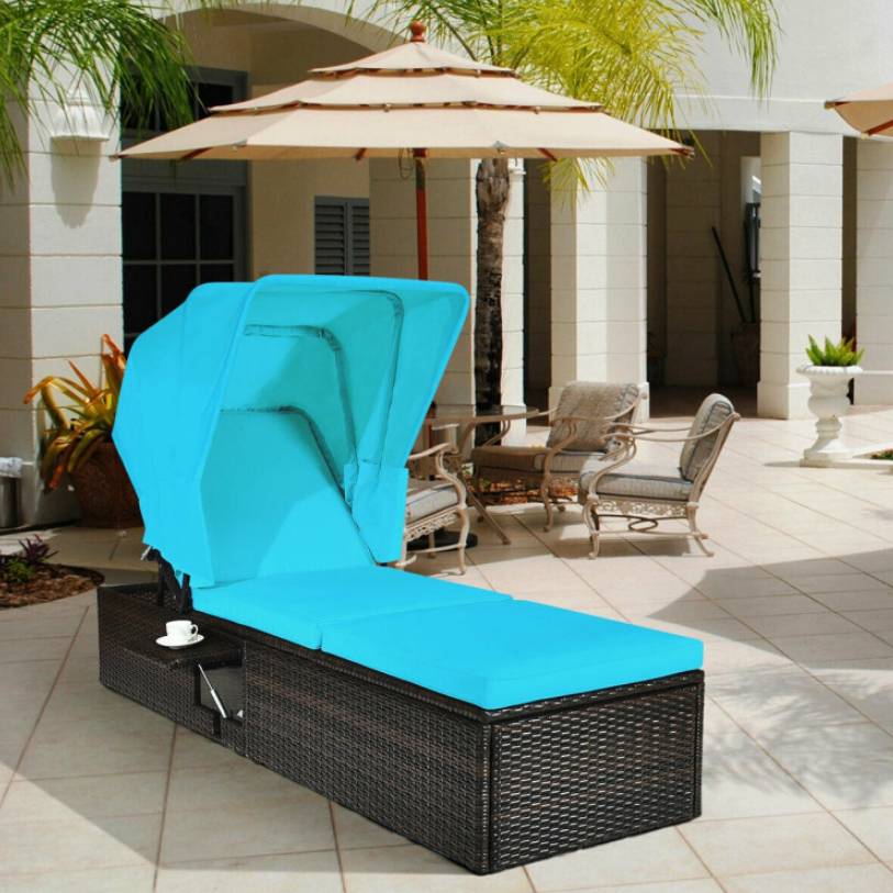 A wicker sun lounger with a blue cushion and adjustable canopy alongside a patio umbrella and outdoor seating set.