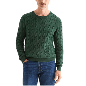 A man is wearing a green cable knit sweater paired with blue jeans. The sweater features a round neckline and ribbed cuffs and hem.