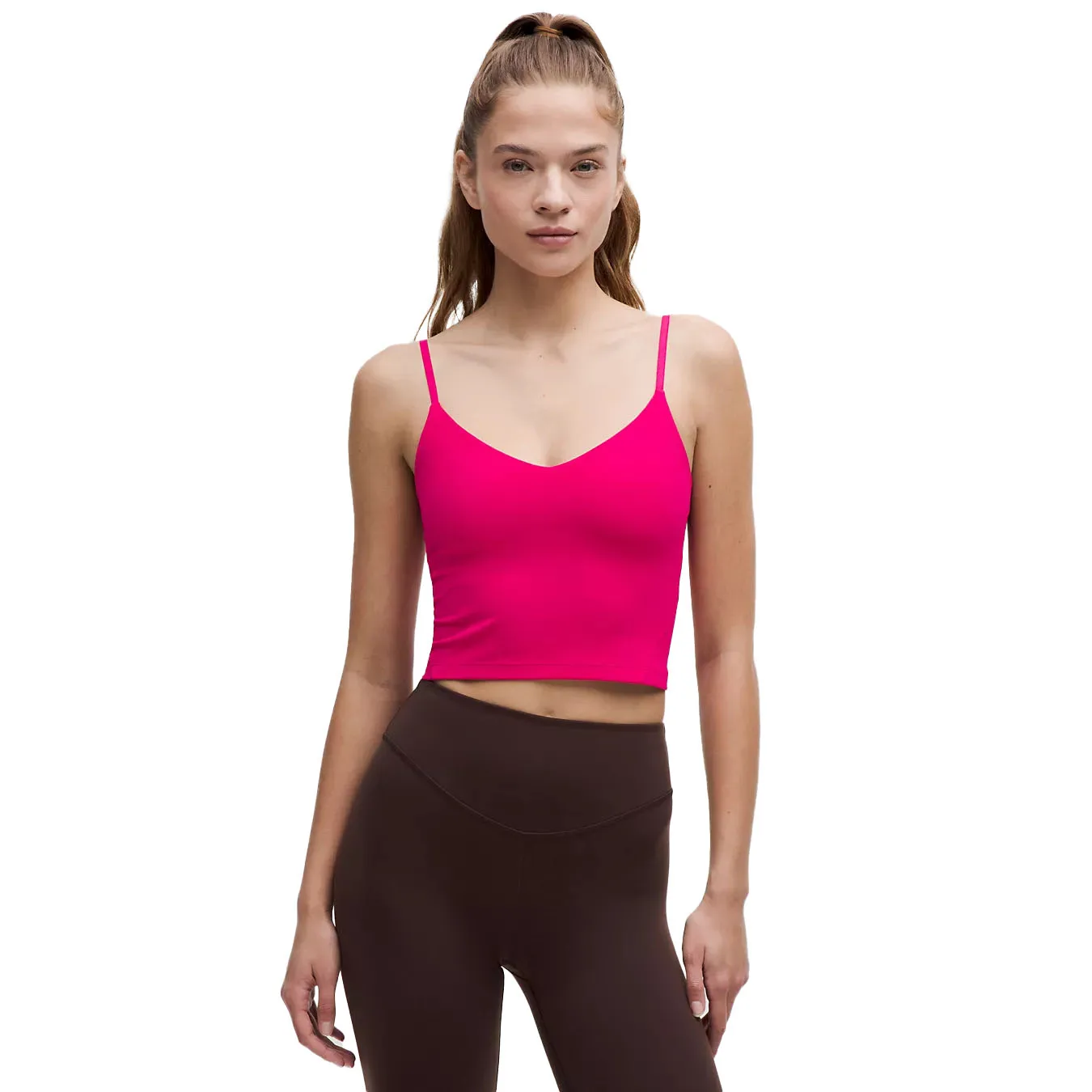 A woman is wearing a bright pink cropped tank top with thin straps, paired with brown high-waisted leggings.