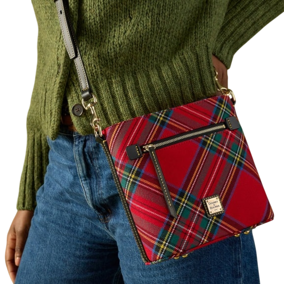 A red tartan plaid crossbody bag with a front zipper pocket and gold hardware is paired with a green knit sweater and denim jeans.