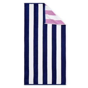 A striped towel with alternating wide vertical navy and white stripes, featuring a corner folded over to reveal pink and white stripes on the reverse side.