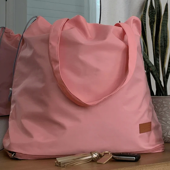 A large pink tote bag is placed on a surface, accompanied by a set of keys with a tassel keychain.