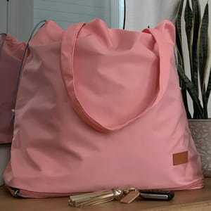 A large pink tote bag is placed on a surface, accompanied by a set of keys with a tassel keychain.