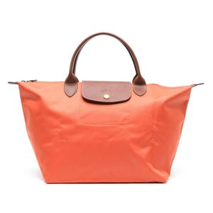 A Longchamp Le Pliage Original Tote in orange with brown leather handles and flap. The tote has a gold button closure and a large, spacious design.