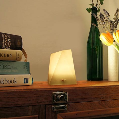 Geometric table lamp, books, green glass vase with flowers on a wooden surface.