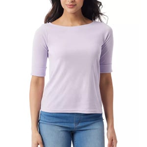 A woman wearing a light purple, elbow-sleeve top with a boat neckline paired with blue jeans.