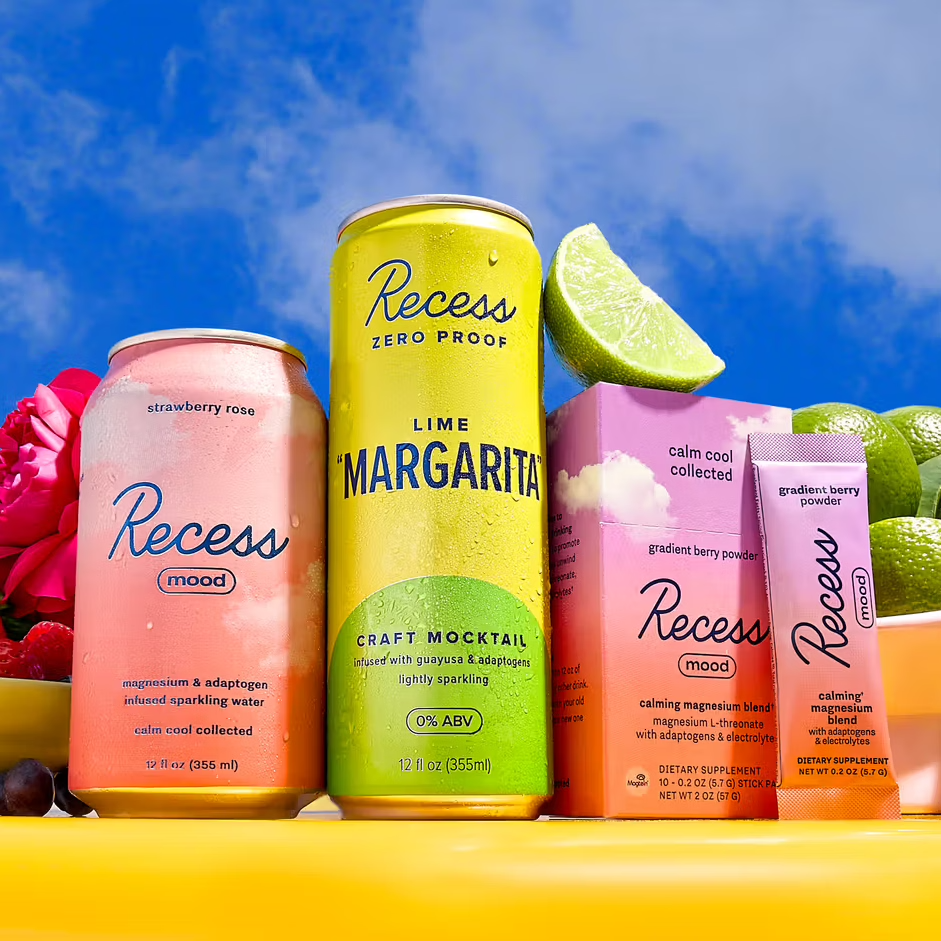 Cans of Recess mood drinks in strawberry rose and lime \“margarita\“ flavors, alongside Recess gradient berry powder packets, are displayed with limes and flowers.