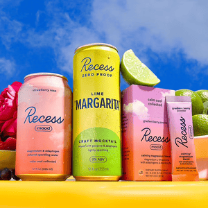 Cans of Recess mood drinks in strawberry rose and lime \“margarita\“ flavors, alongside Recess gradient berry powder packets, are displayed with limes and flowers.